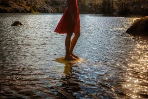 Low section of woman in red dress at lake