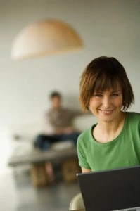 Smiling woman using laptop computer, man in the background